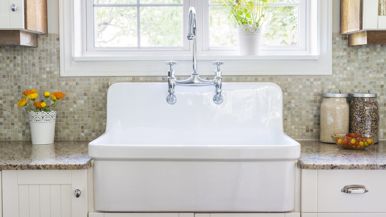 Farmhouse sink with chrome faucet mounted in cream cabinets