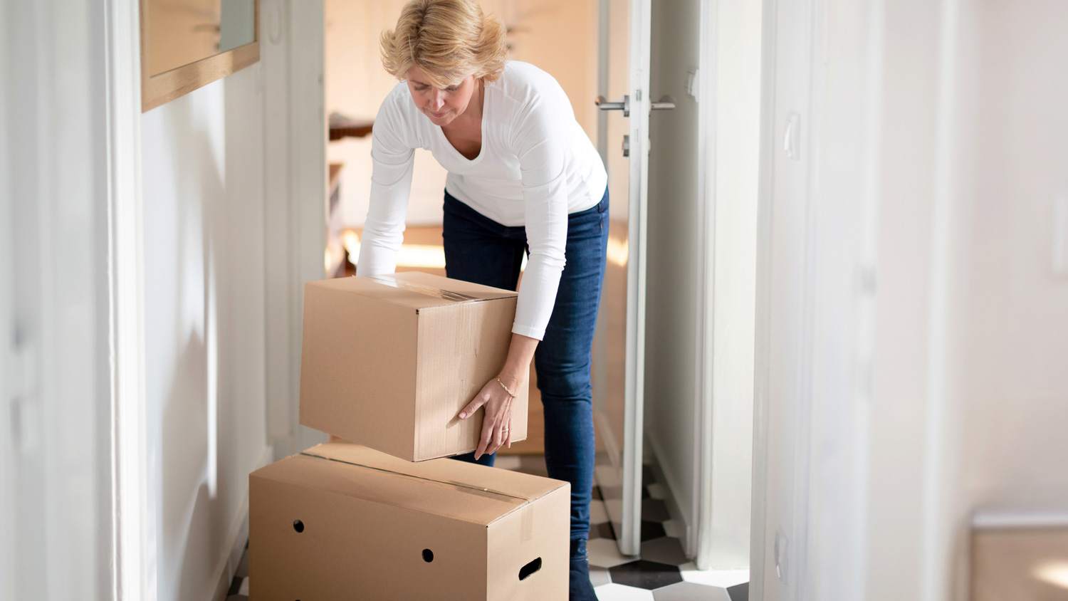 A woman lifting boxes from her new house’s corridor