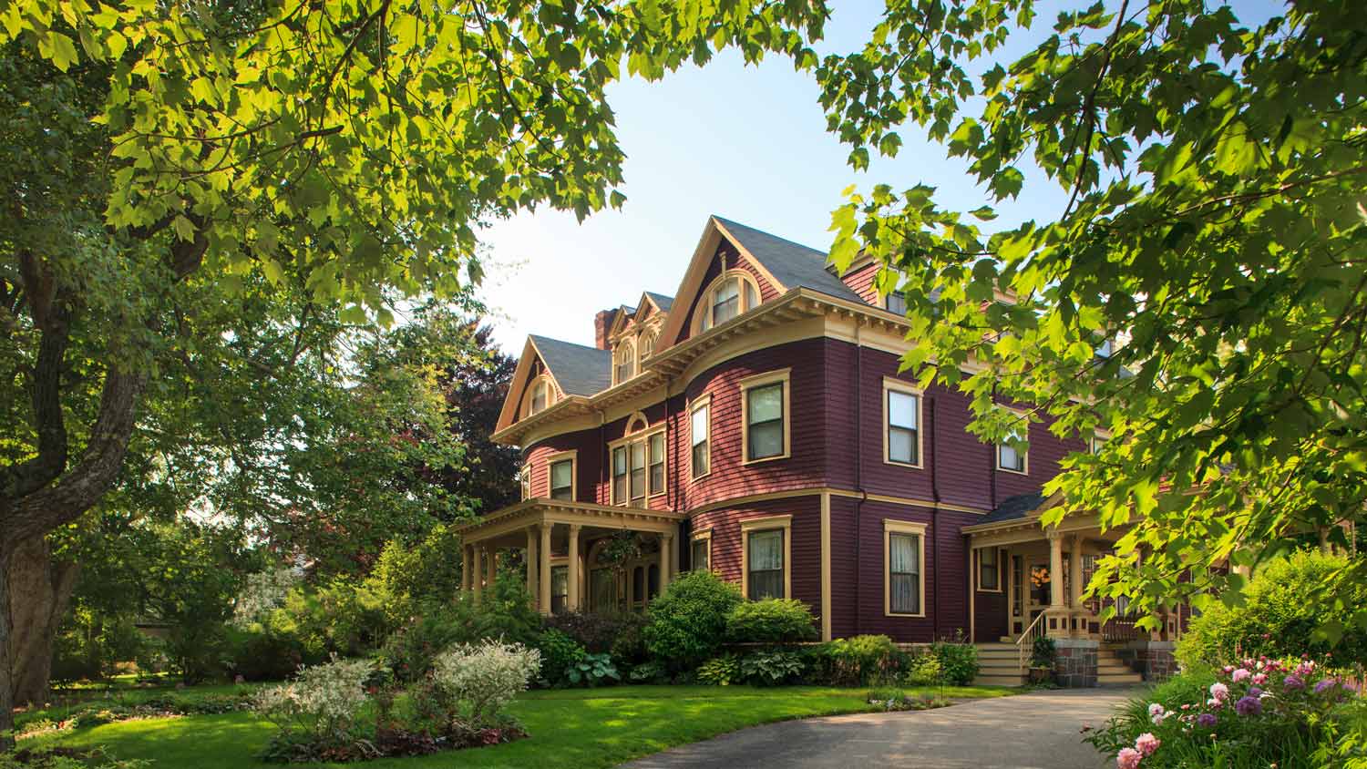 The facade of a Victorian mansion surrounded by gardens