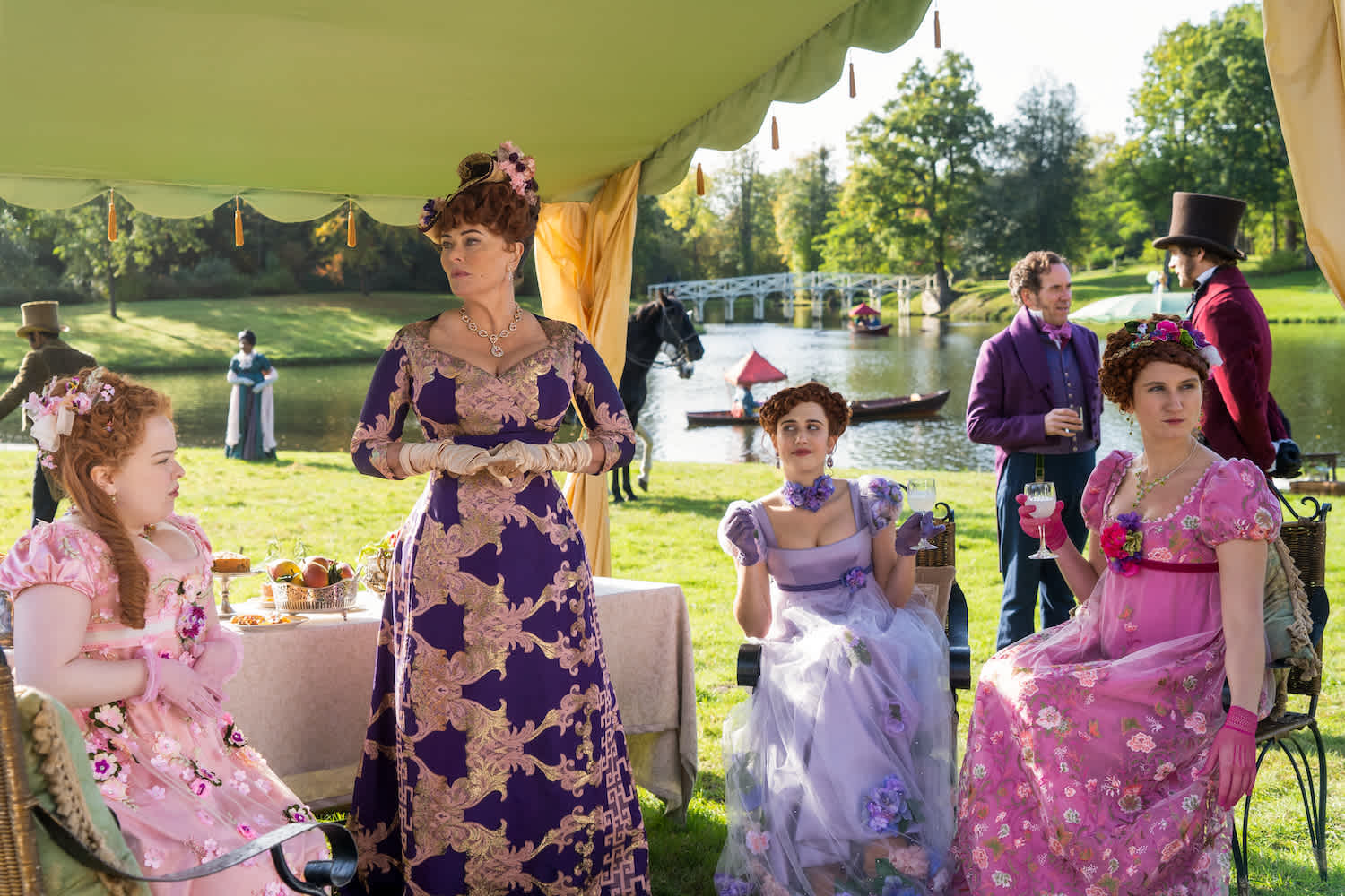 Ornately dressed Regency era women having tea by a pond