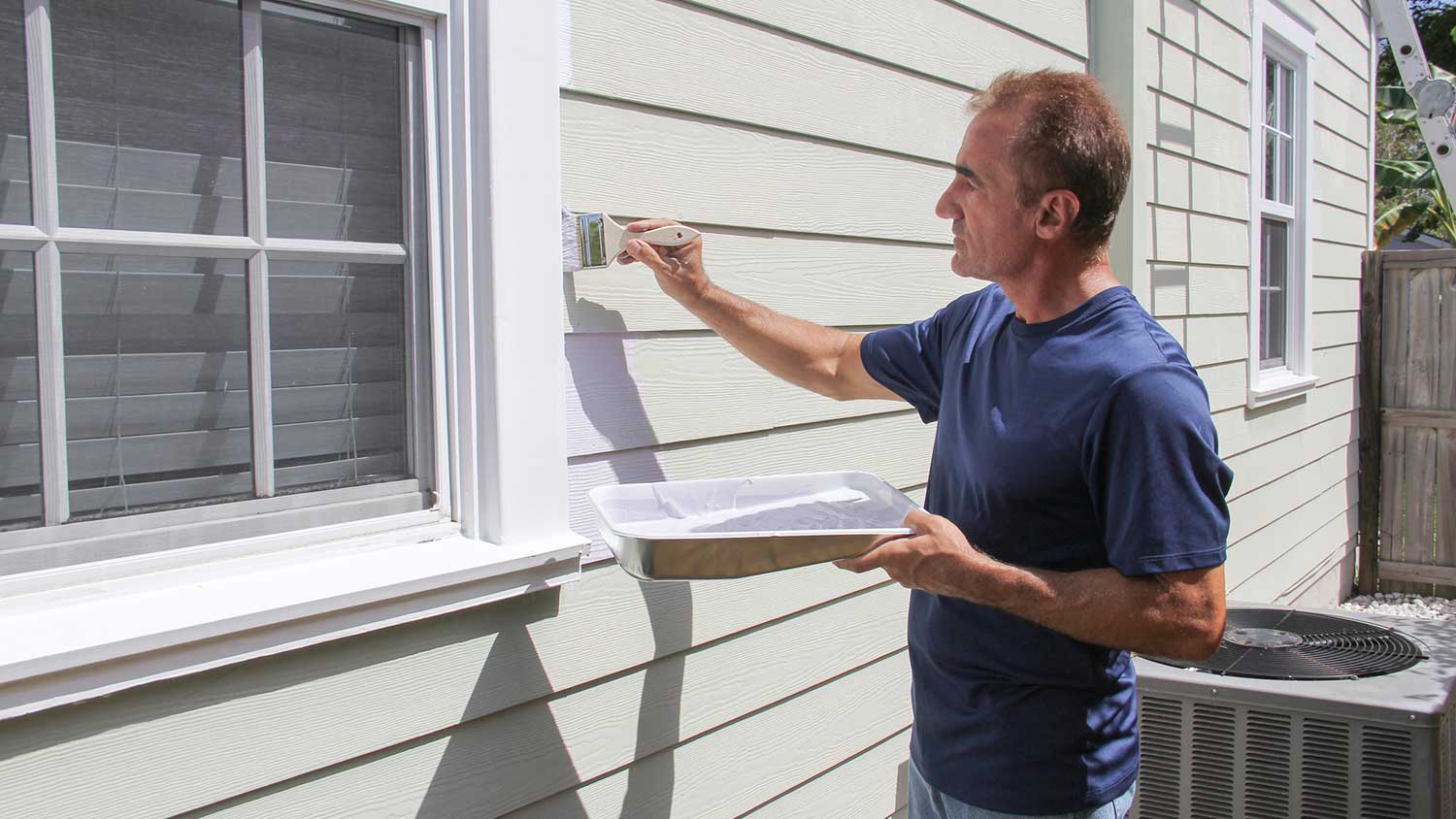 Man painting house siding with a brush
