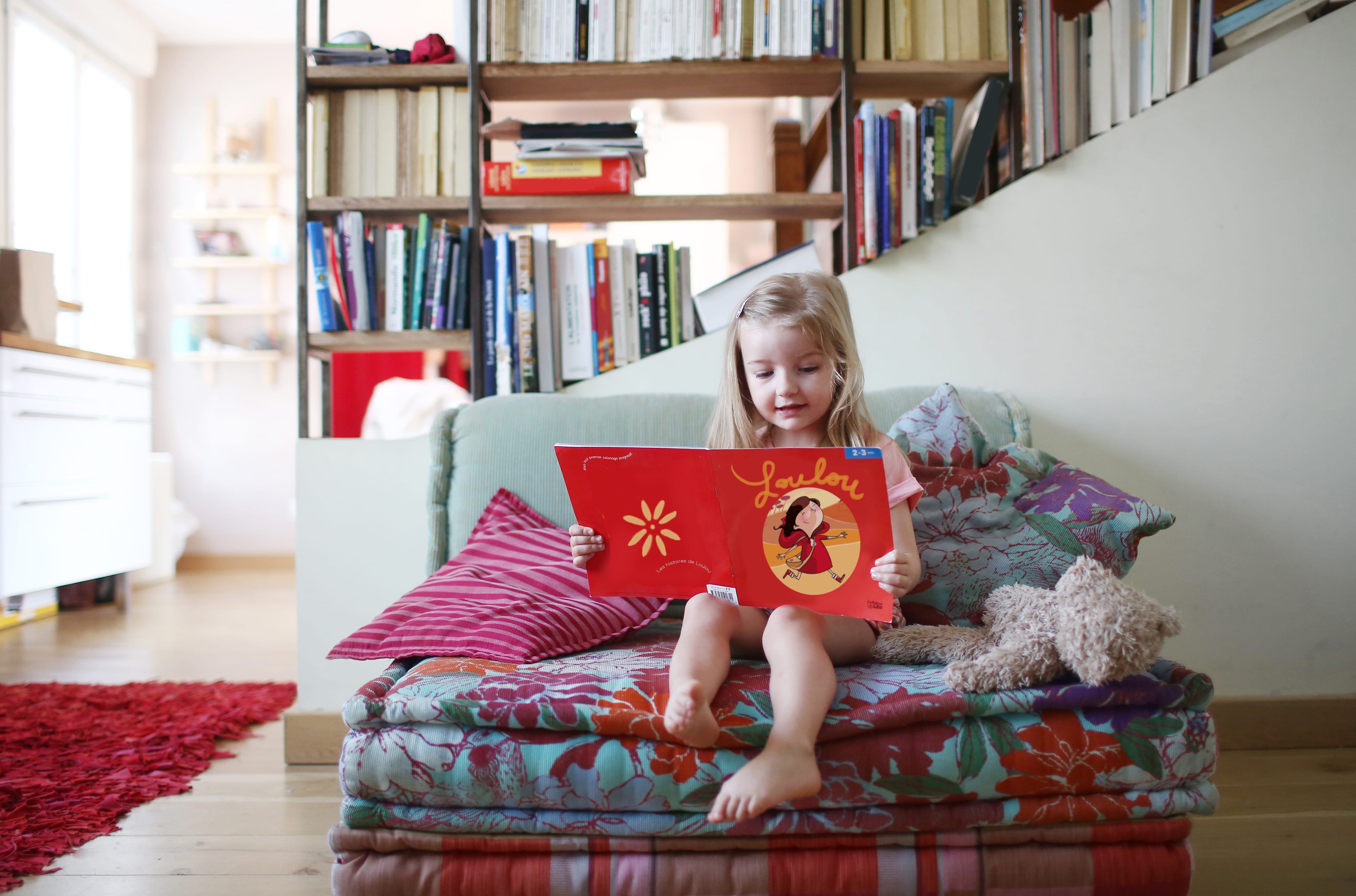 Girl reading a book next to bookshelf