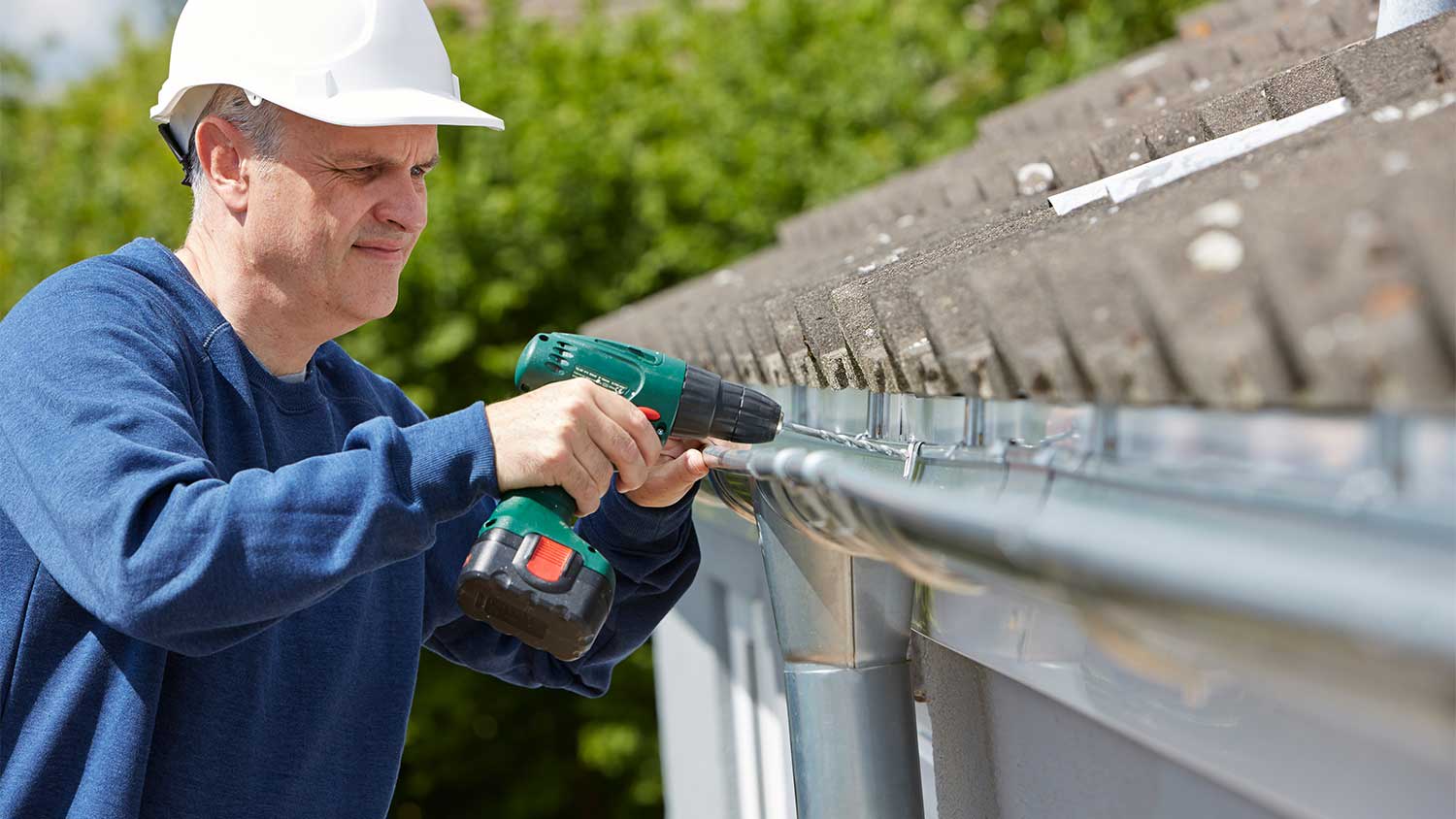 Worker using a drill is fixing house gutter