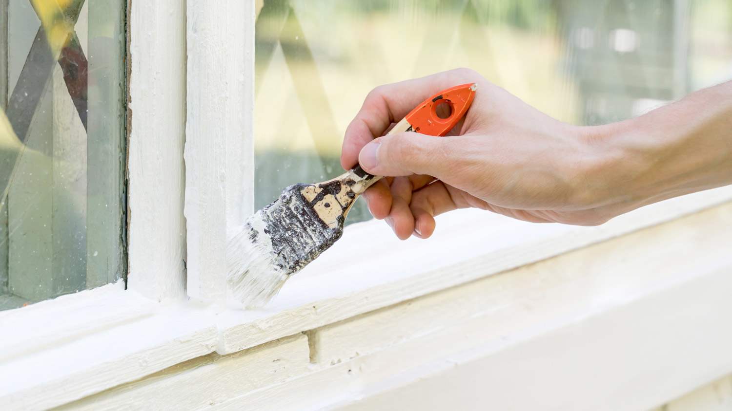 Close-up of a hand painting with a brush the window’s exterior frame