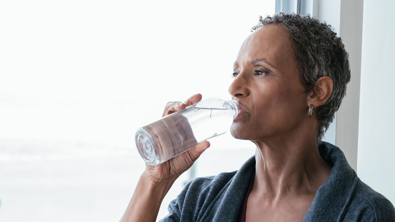 Woman by the window drinking water from a bottle