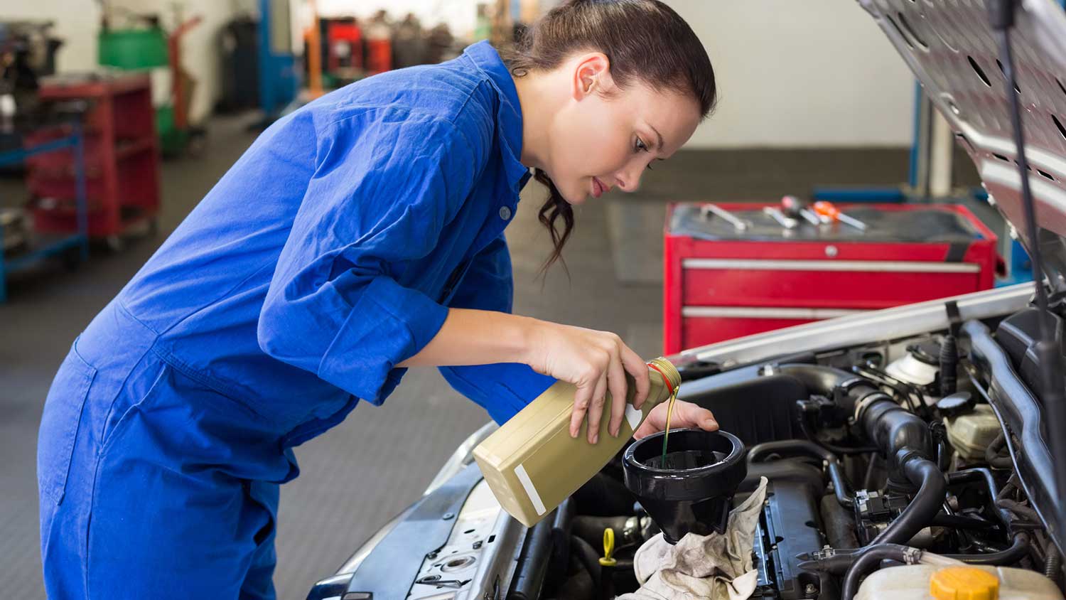 Female auto mechanic adding oil to a car
