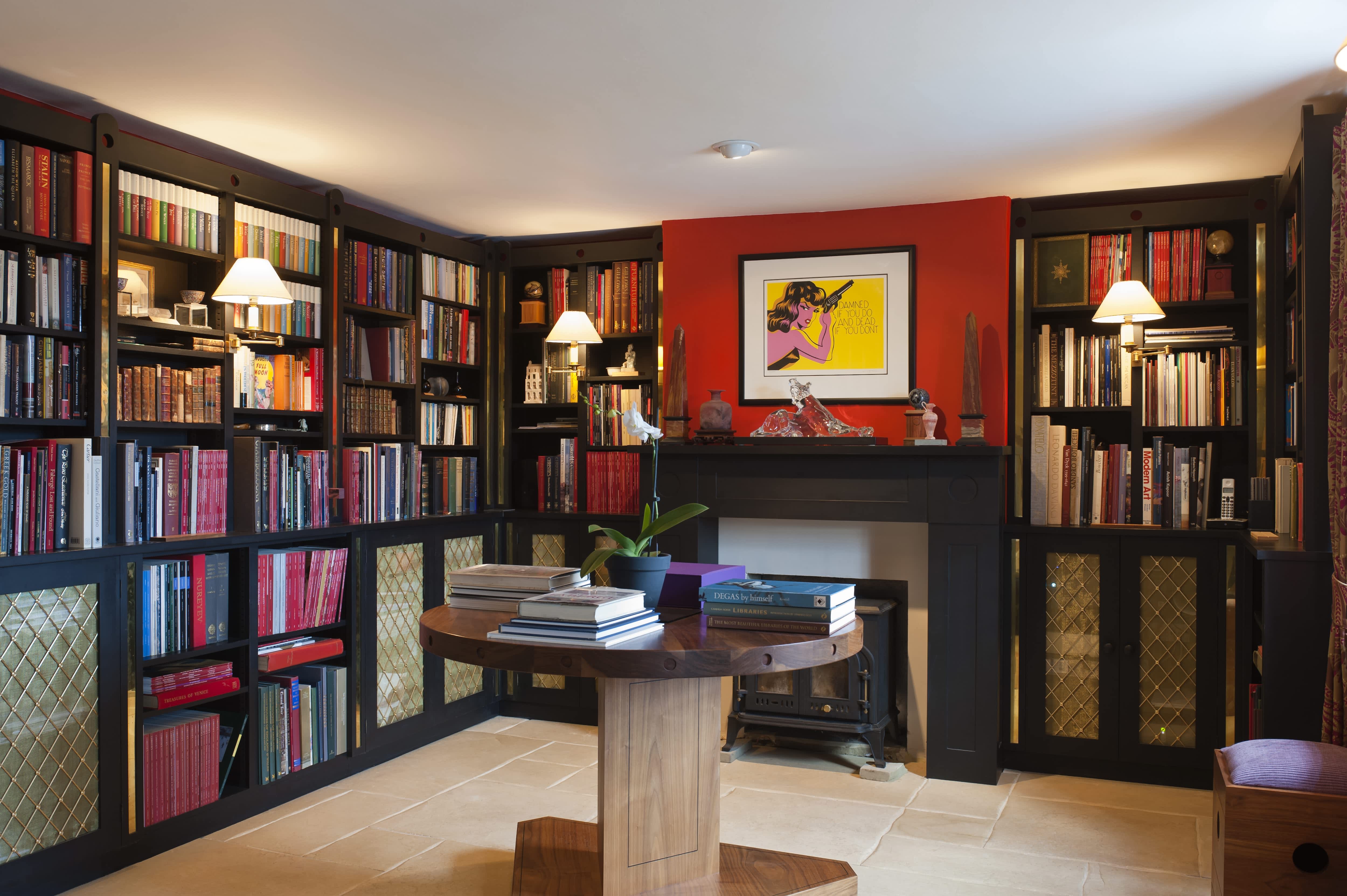 Home library with black bookshelves, round wooden table, and fireplace with red chimney and Niagara Detroit pop art print