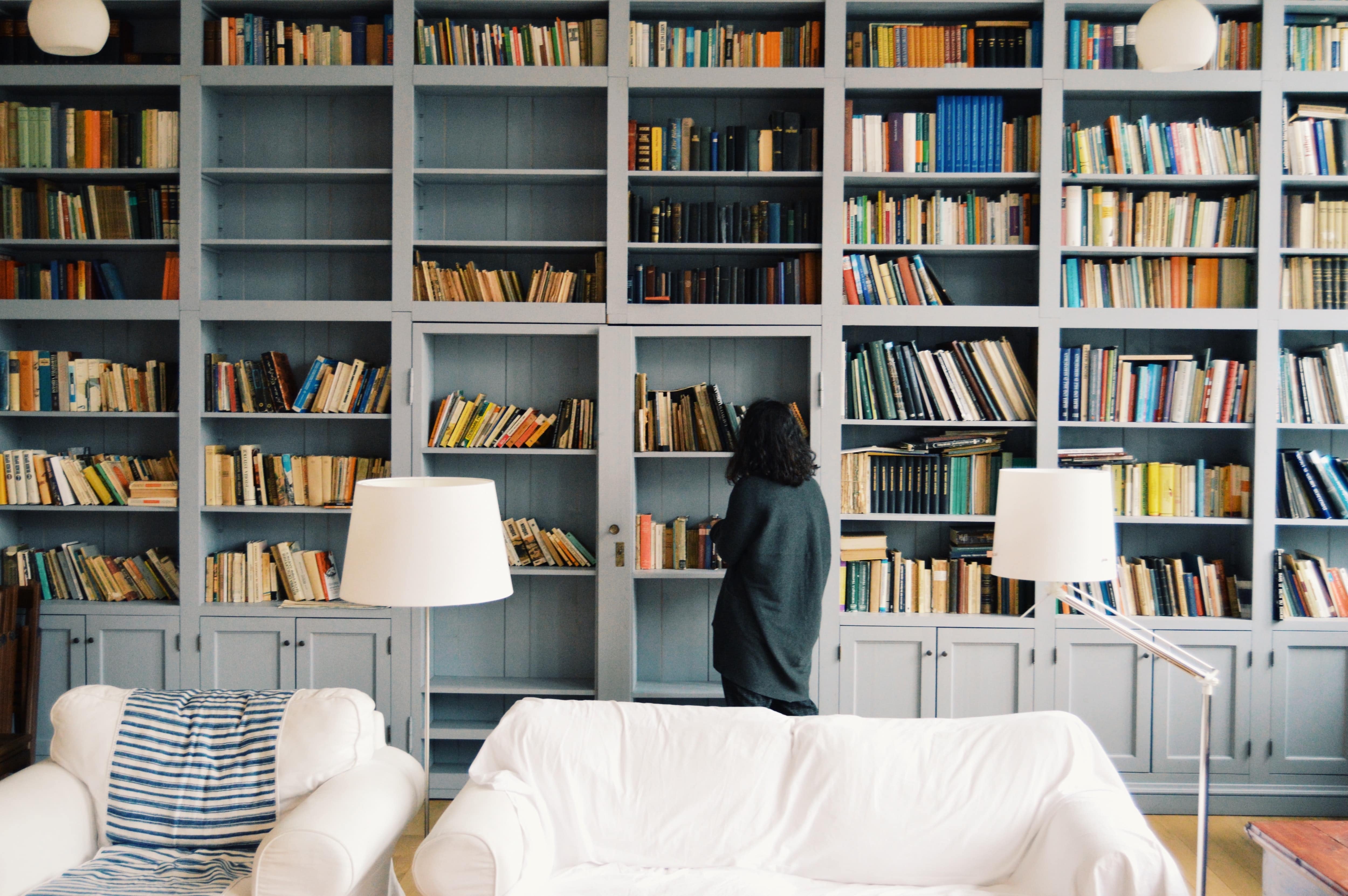Woman browsing books in her home library with dove gray floor to ceiling bookshelves