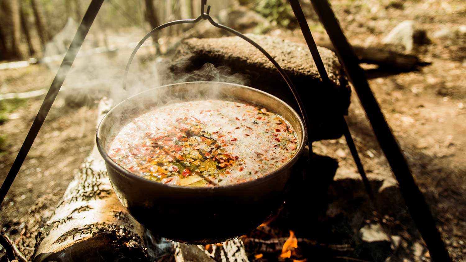 Closeup of big pot with soup cooking over campfire