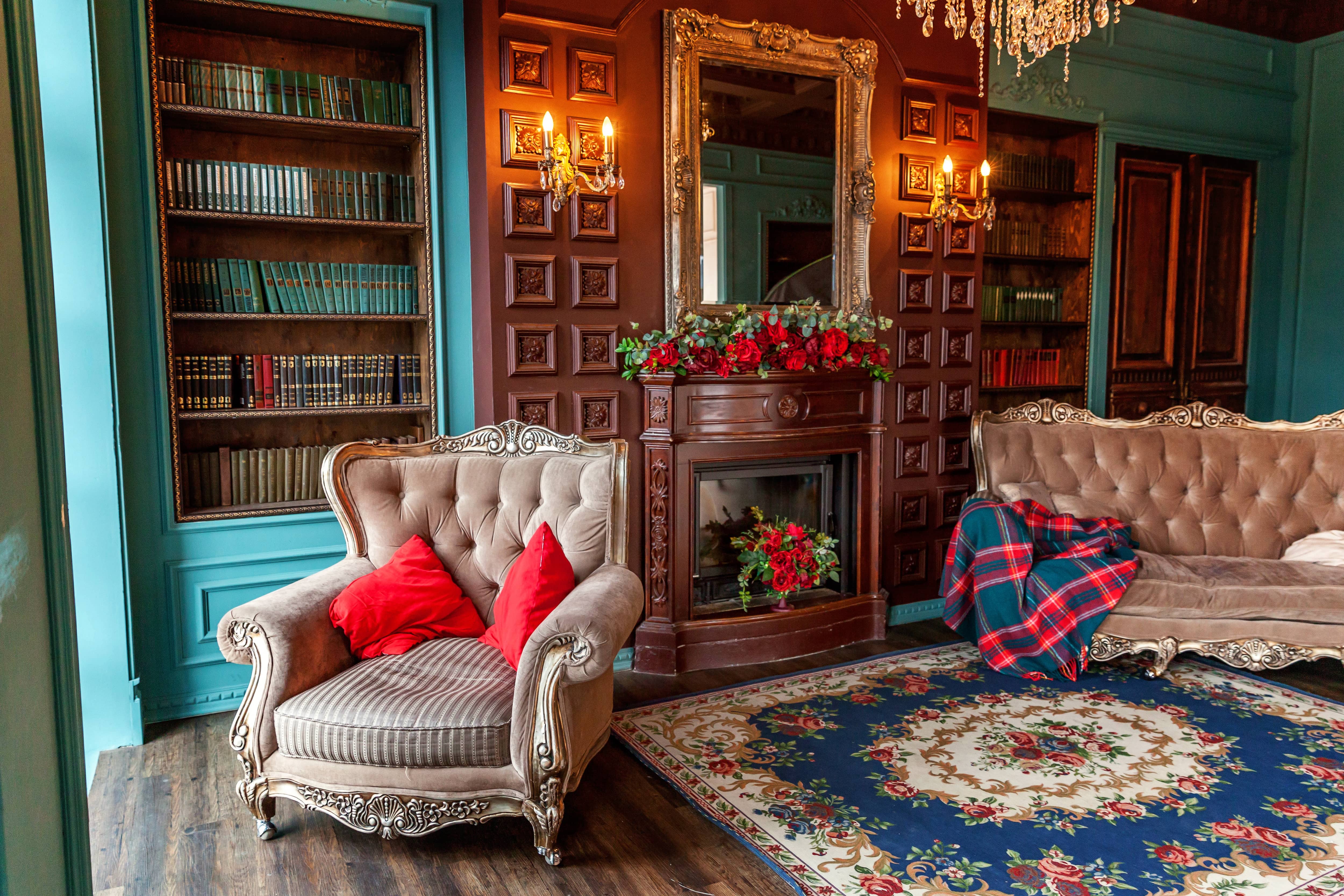 Home library with green walls, wooden built-in bookshelves, fireplace, blue floral rug, and a taupe tufted arm chair and sofa