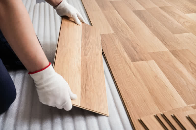 white gloved hands laying laminate wood boards on top of gray foam