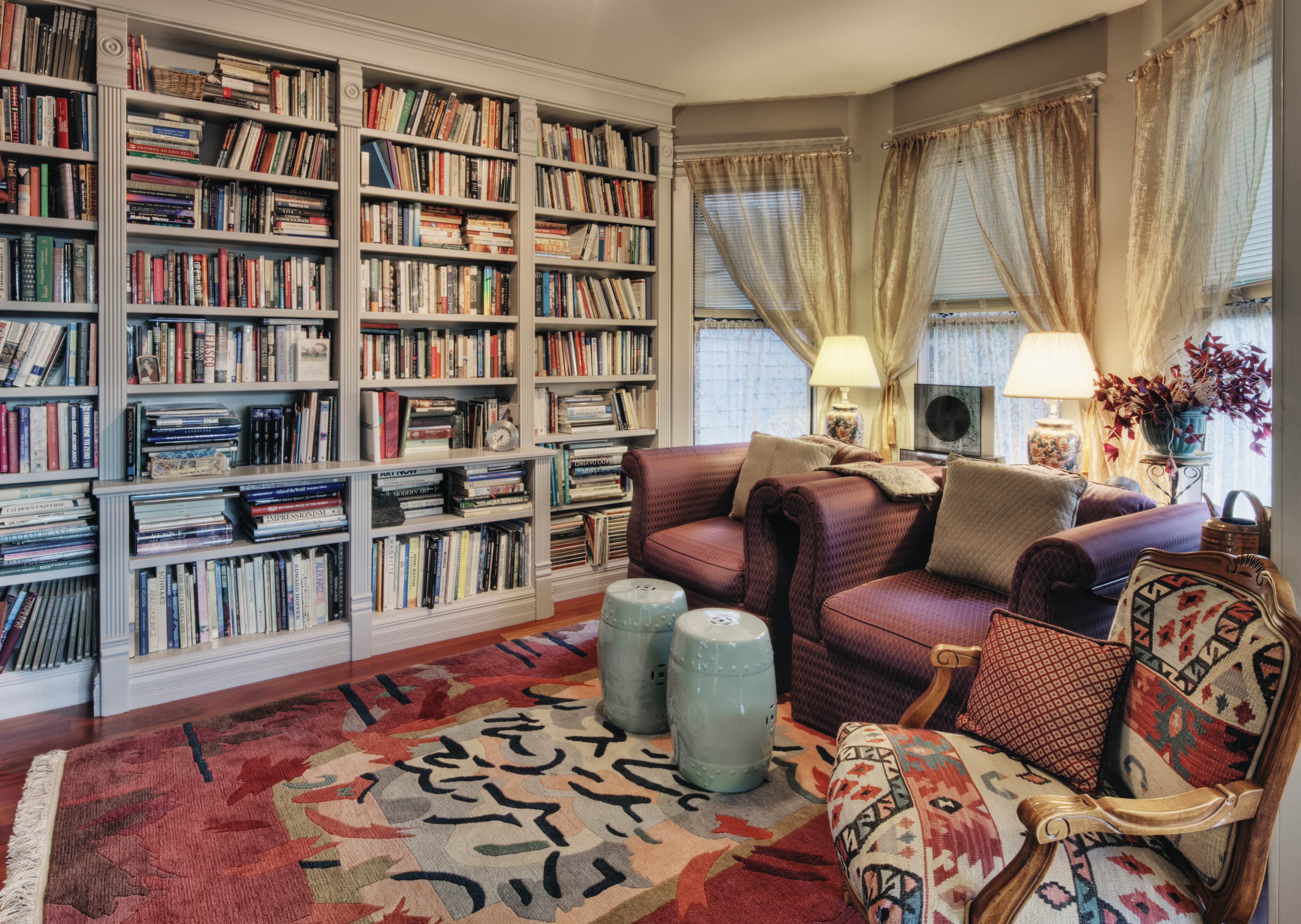 Home library with gray bookshelves, patterned rug, and South West upholstered chair
