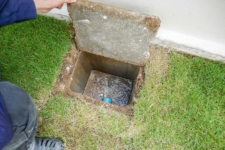 an arm holds opening a square sewer opening for a home