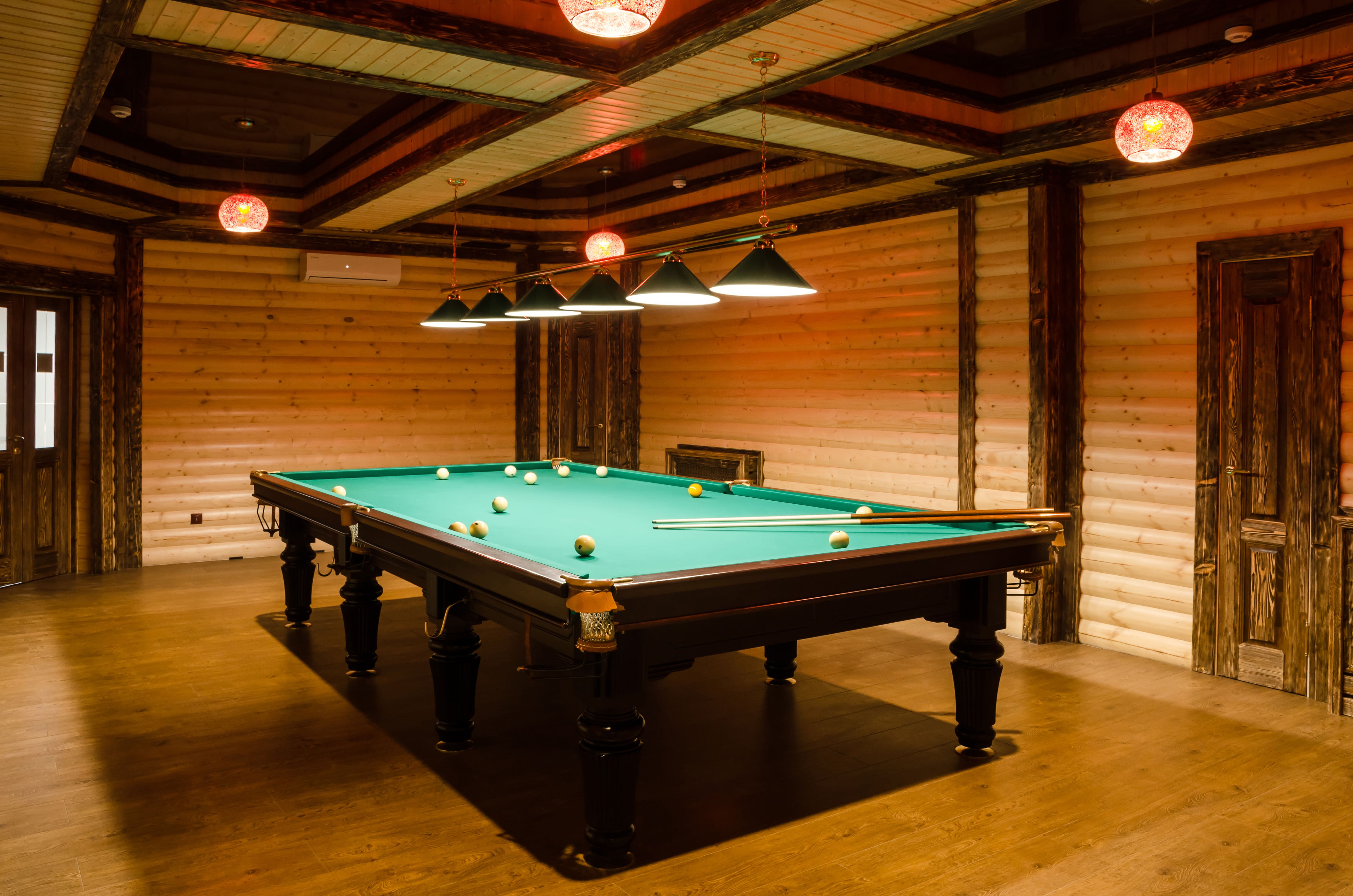 A basement room with a billiards table and wood plank ceiling