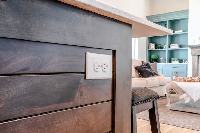 closeup of electrical outlet in kitchen island with living room furniture in the background