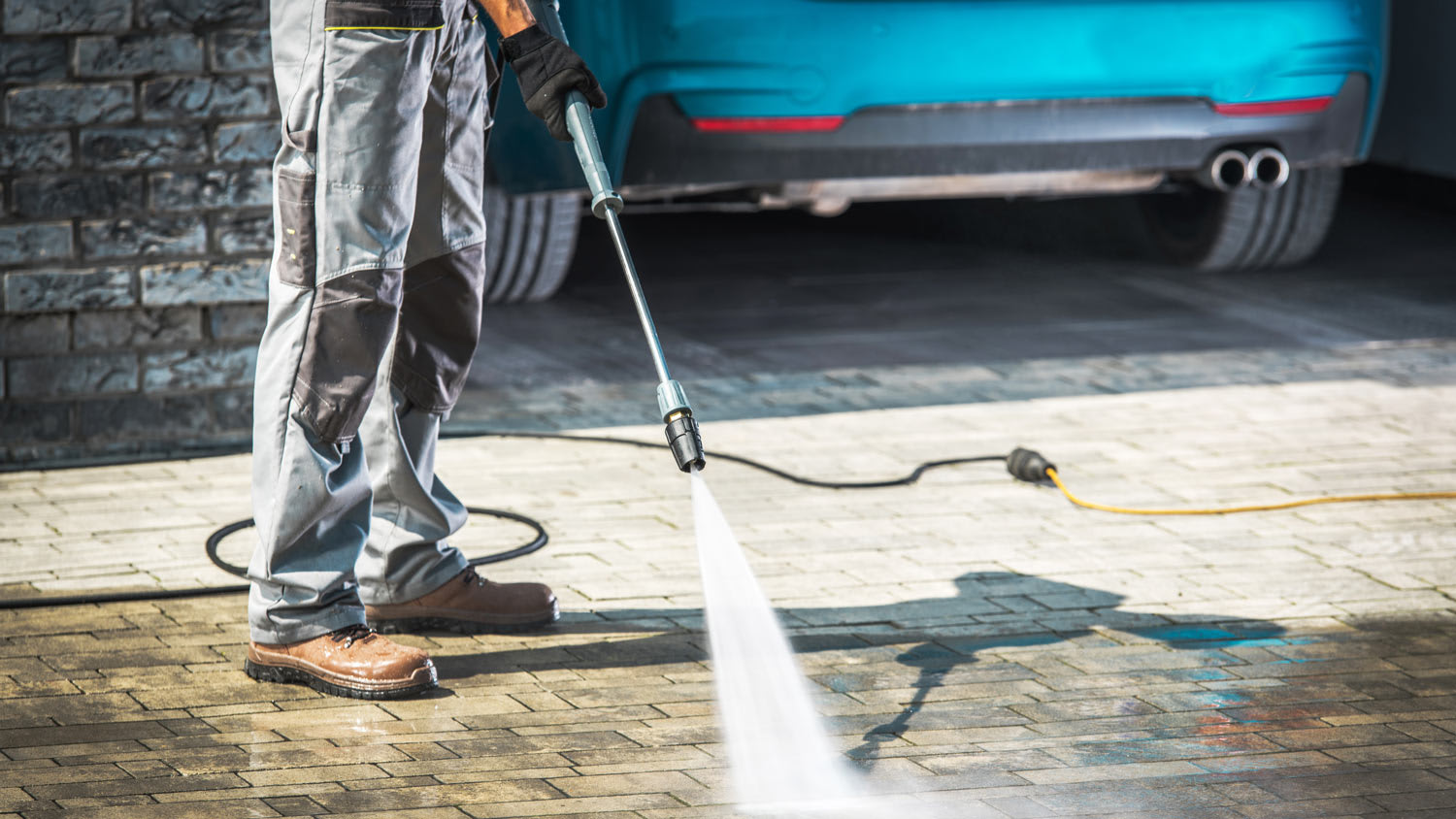 A man cleans his home’s driveway using a pressure washer