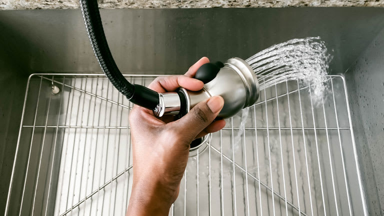 High-angle view of woman rinsing down kitchen sink with faucet hose sprayer