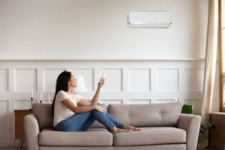 woman on couch using remote to adjust air conditioner