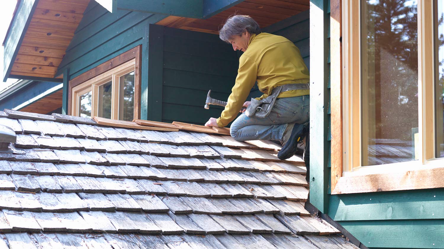 Roofer patches cedar shingles at roof ridgeline
