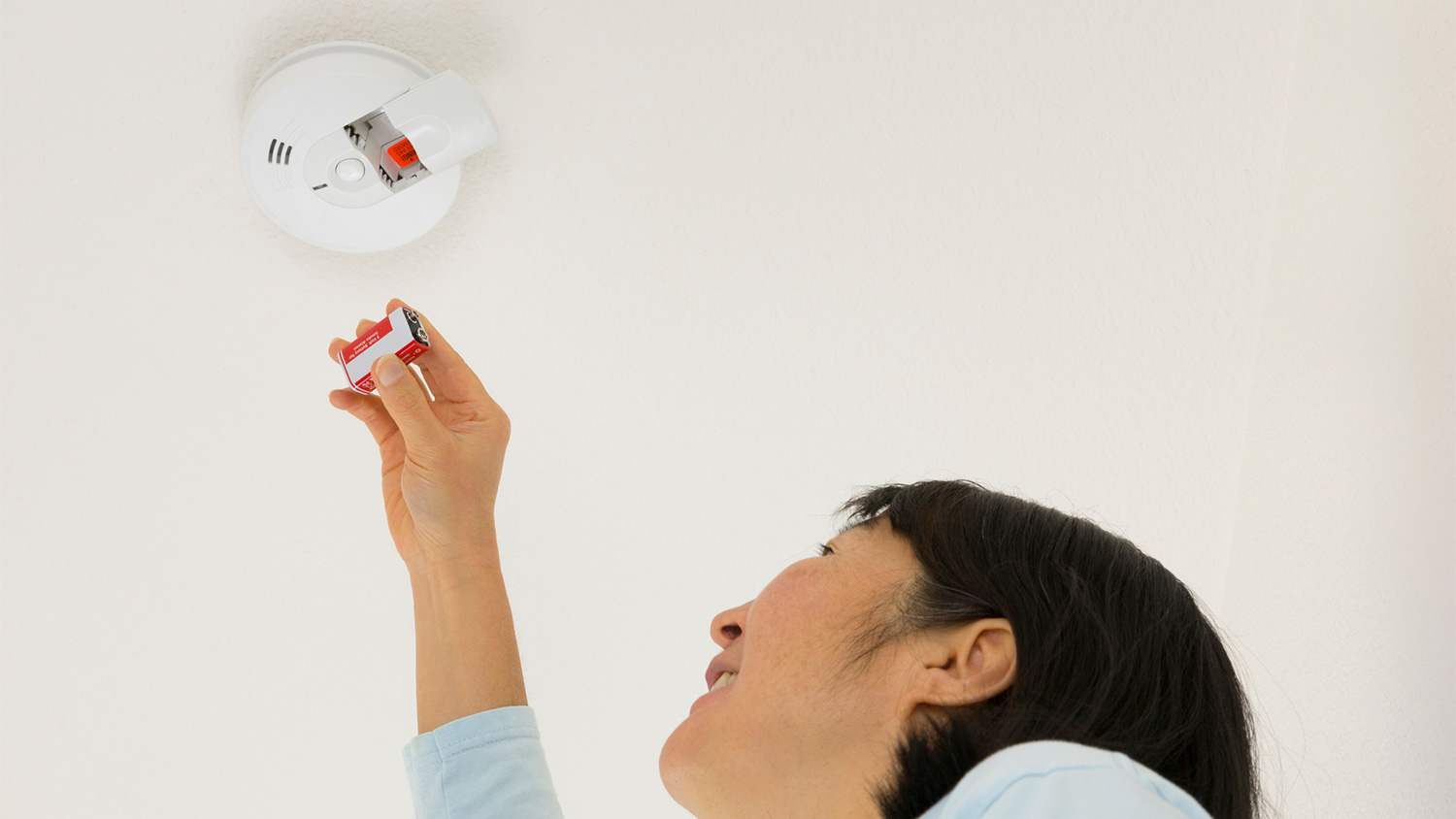 Woman inserting battery in smoke detector