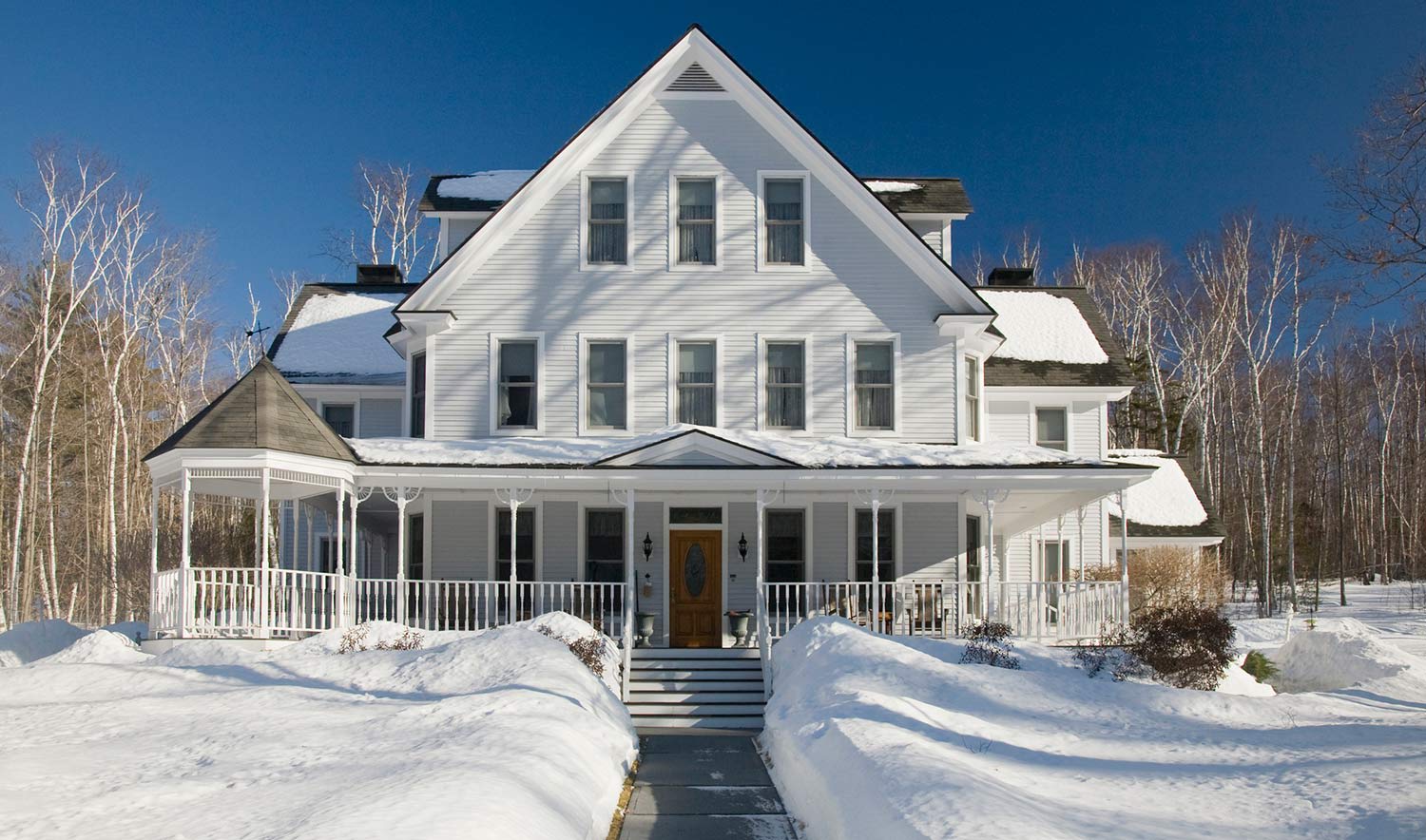 Home with wraparound porch surrounded by snow
