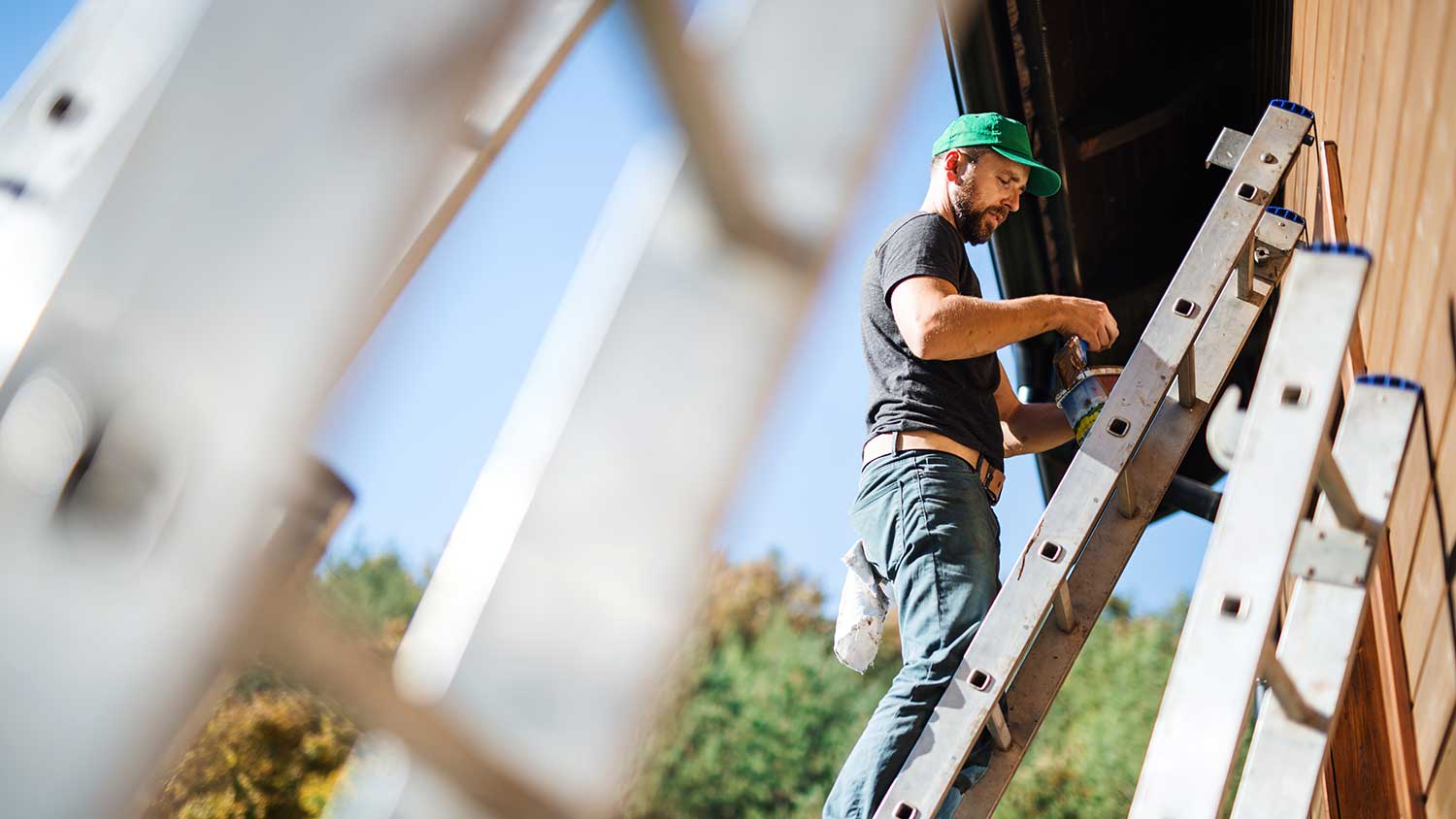 Man using a ladder to paint house exterior