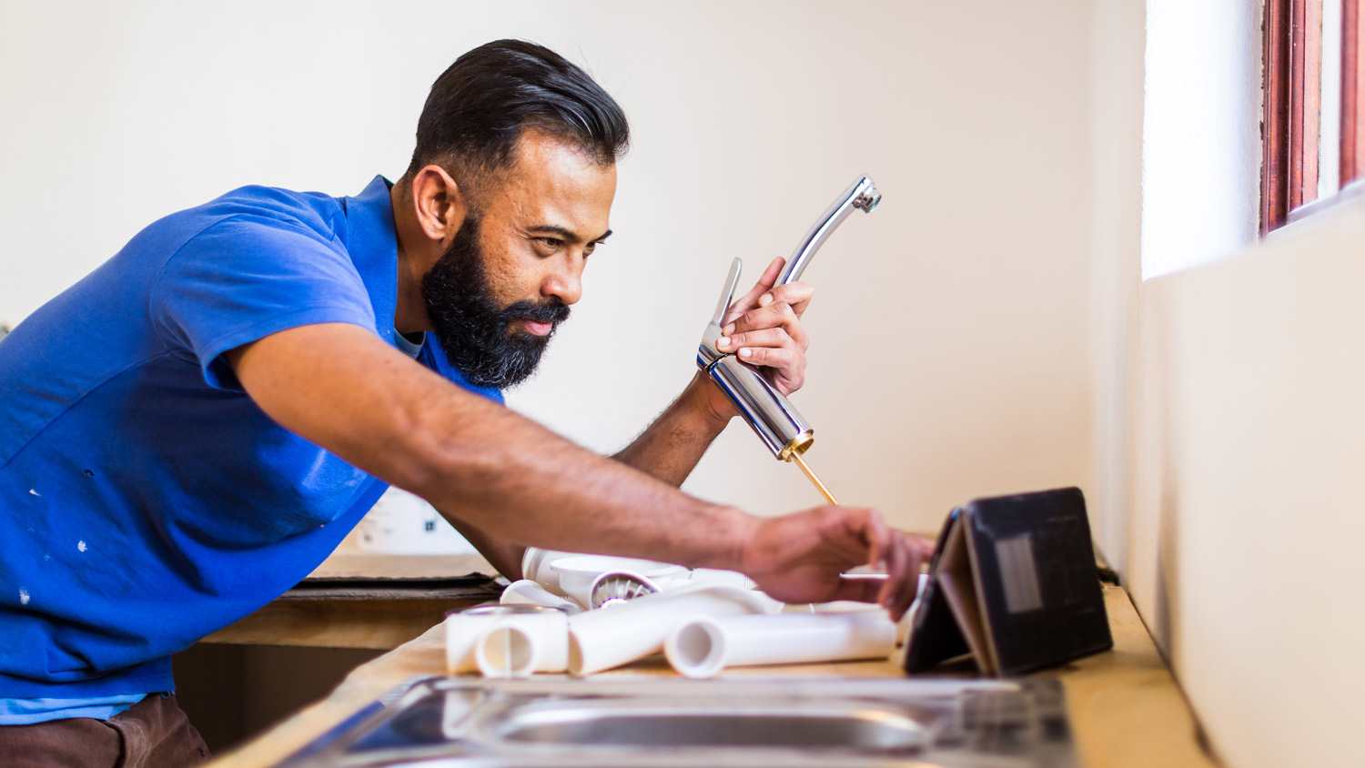 A plumber changing a faucet while checking his tablet