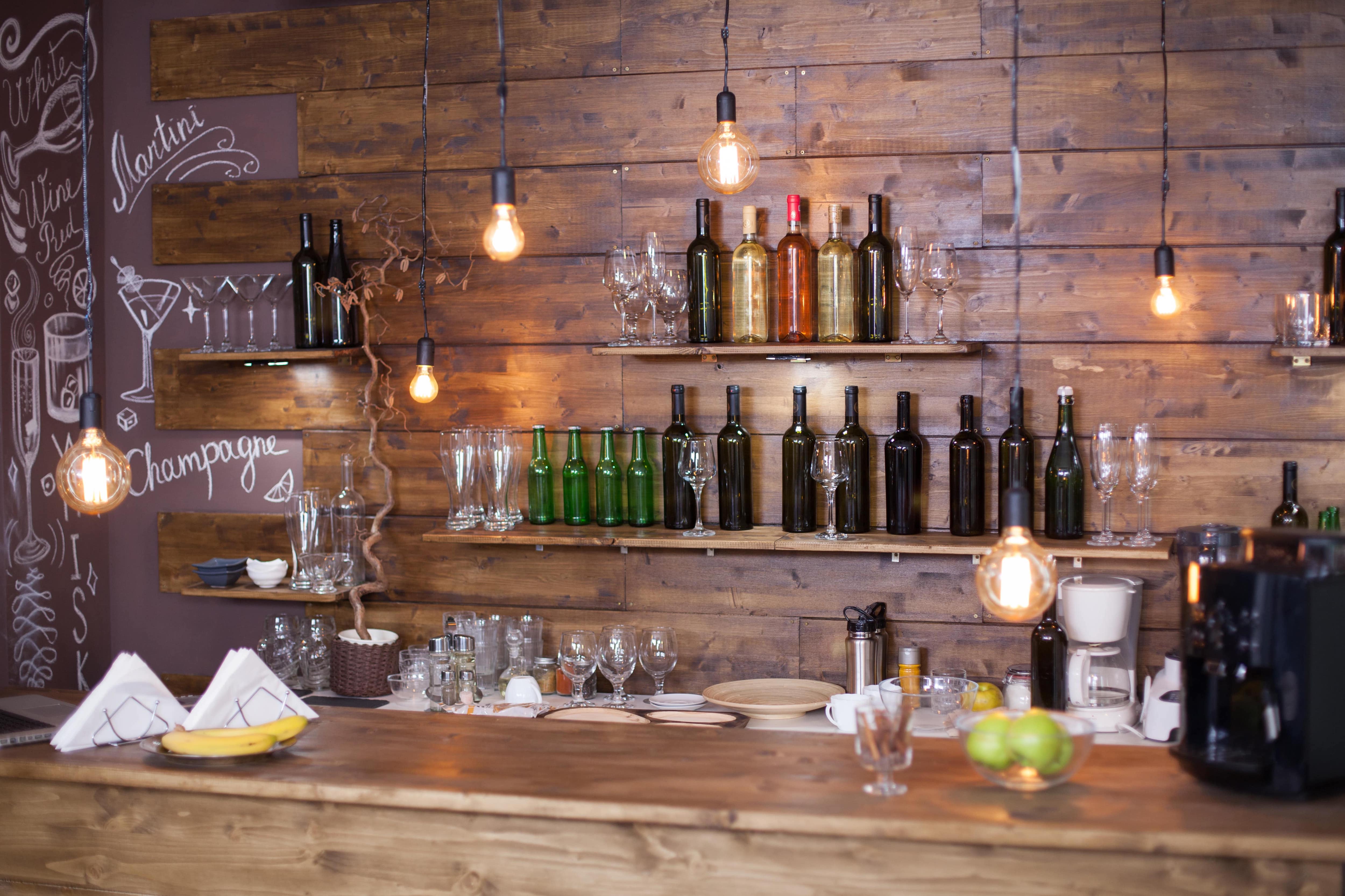 Rustic basement bar with shiplap walls, Edison bulbs, and vintage wine bottles on open shelves