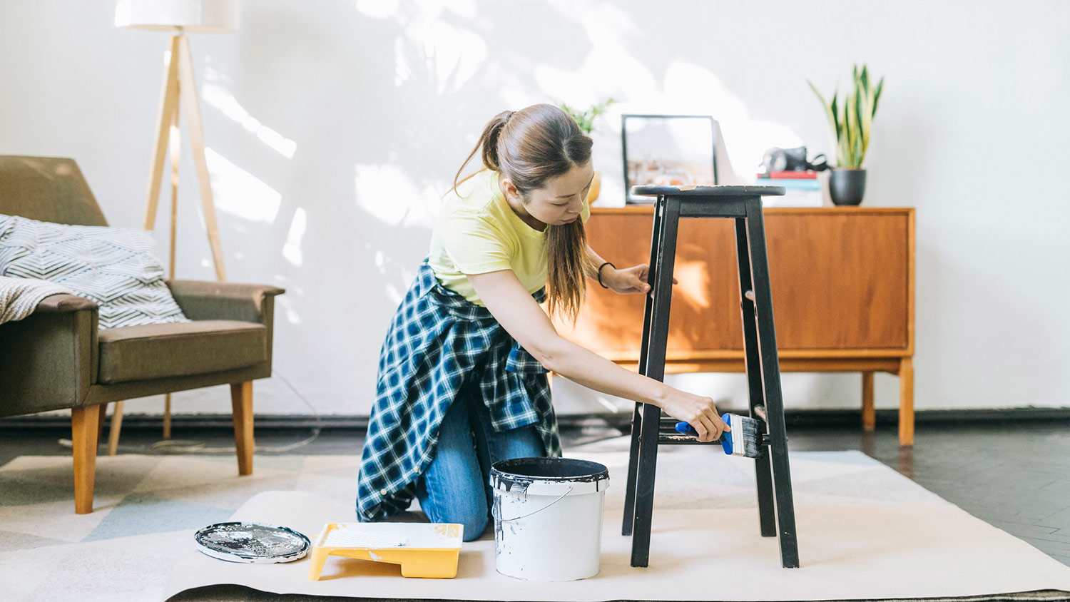 A woman paints a wood barstool black in her apartment