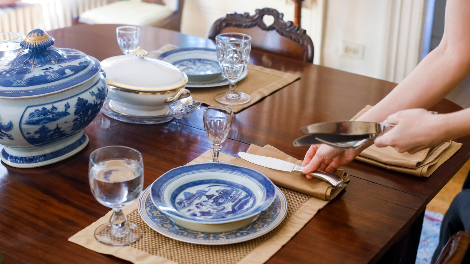 A woman’s hand setting the table with antique tableware