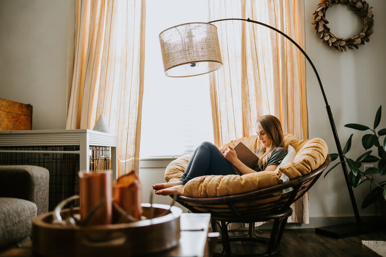 Woman reading indoors in rattan chair