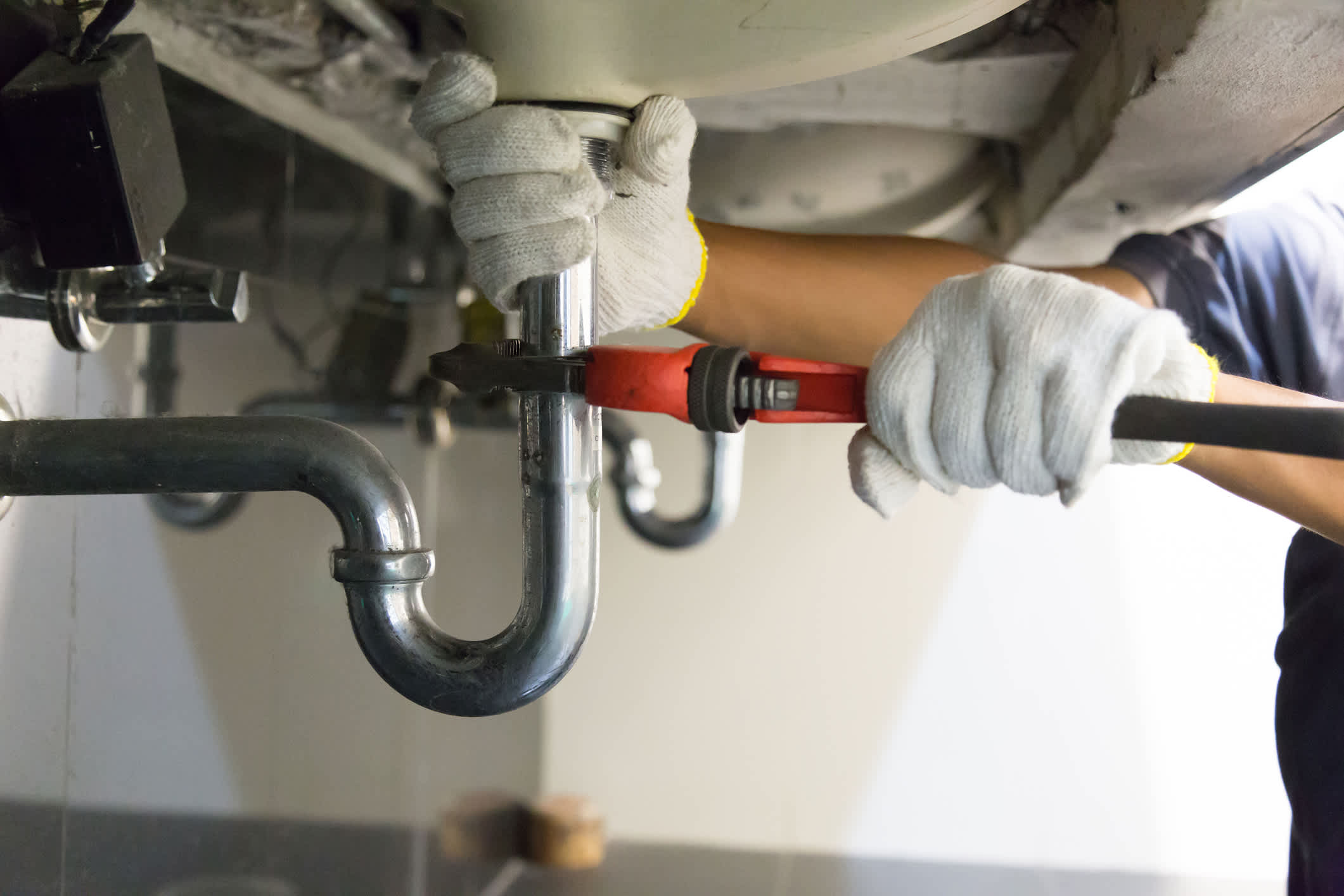 A plumber’s hands in gloves fixing a bathroom’s sink pipes