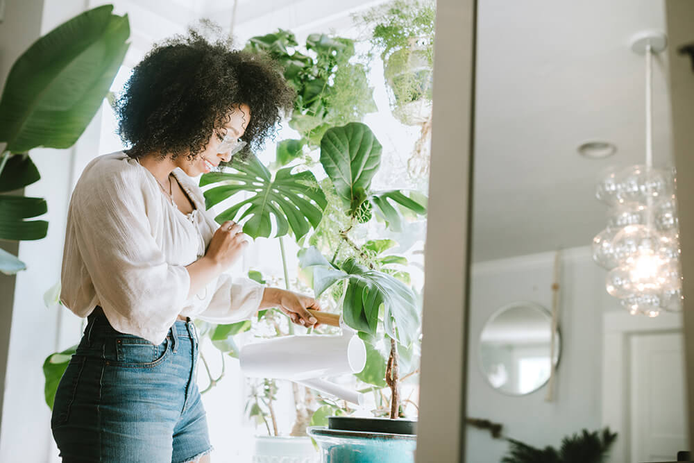 Woman watering plants in front of a large window