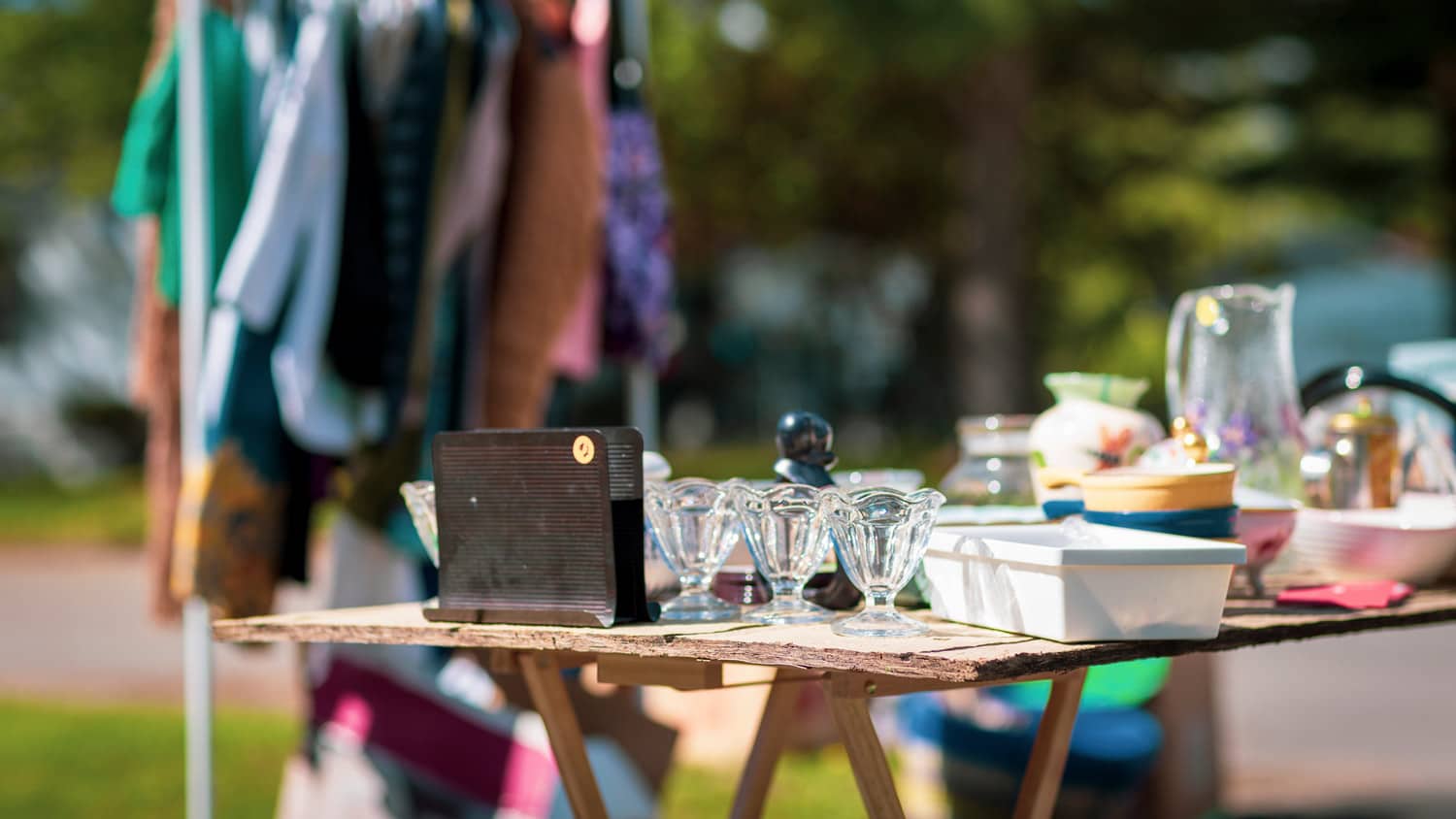 A garage sale with vintage glassware and clothes in the background