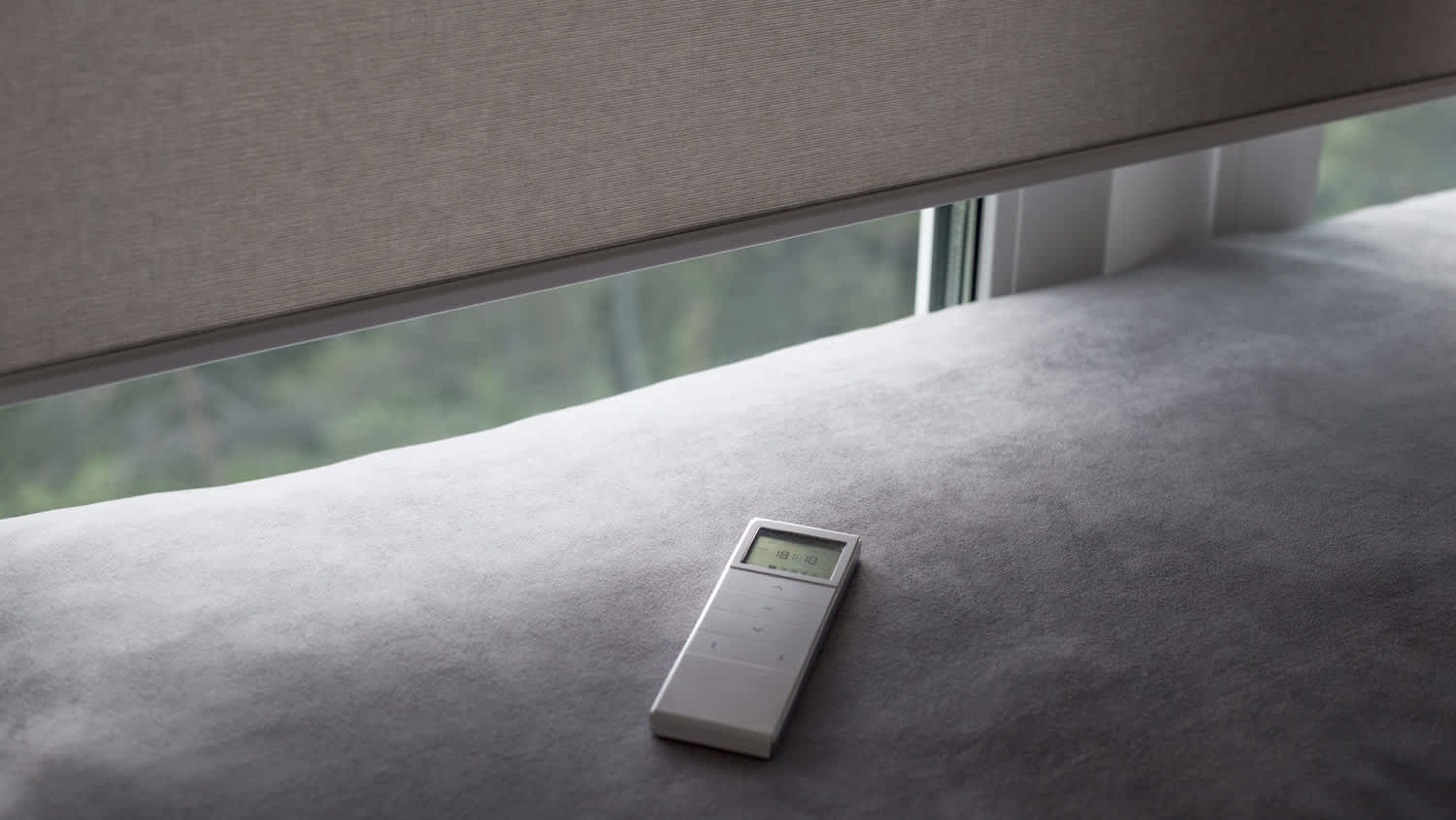 Motorized window roller blinds with the remote controller on a sofa