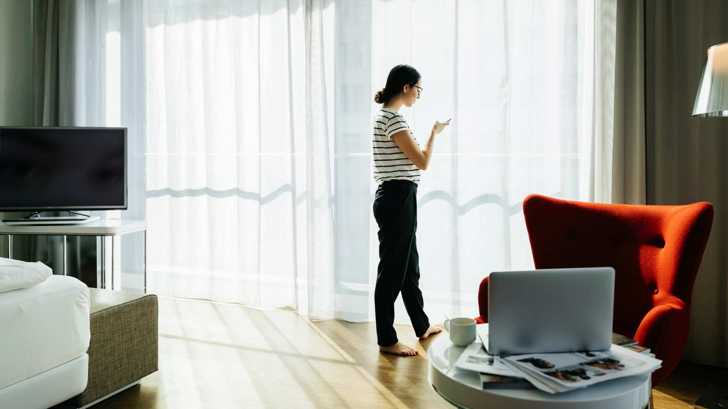A woman standing in front of a tall window with draperies