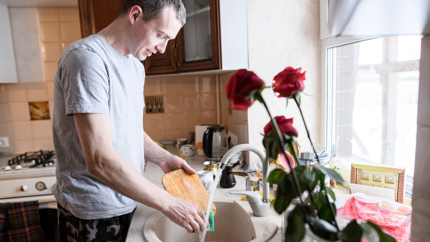 A young man washing cutting board in kitchen sink