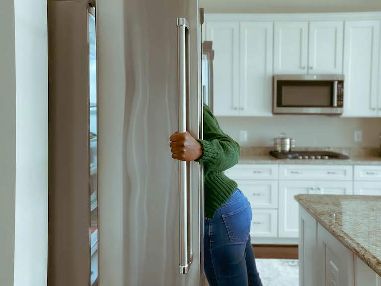 view from side of fridge of woman looking inside, mostly blocked by silver door