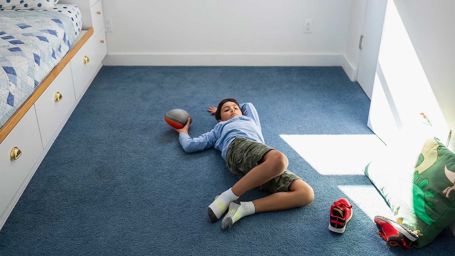Boy holding a ball lying on carpet in his bedroom