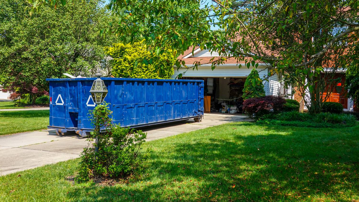 A blue dumpster in the driveway of a house