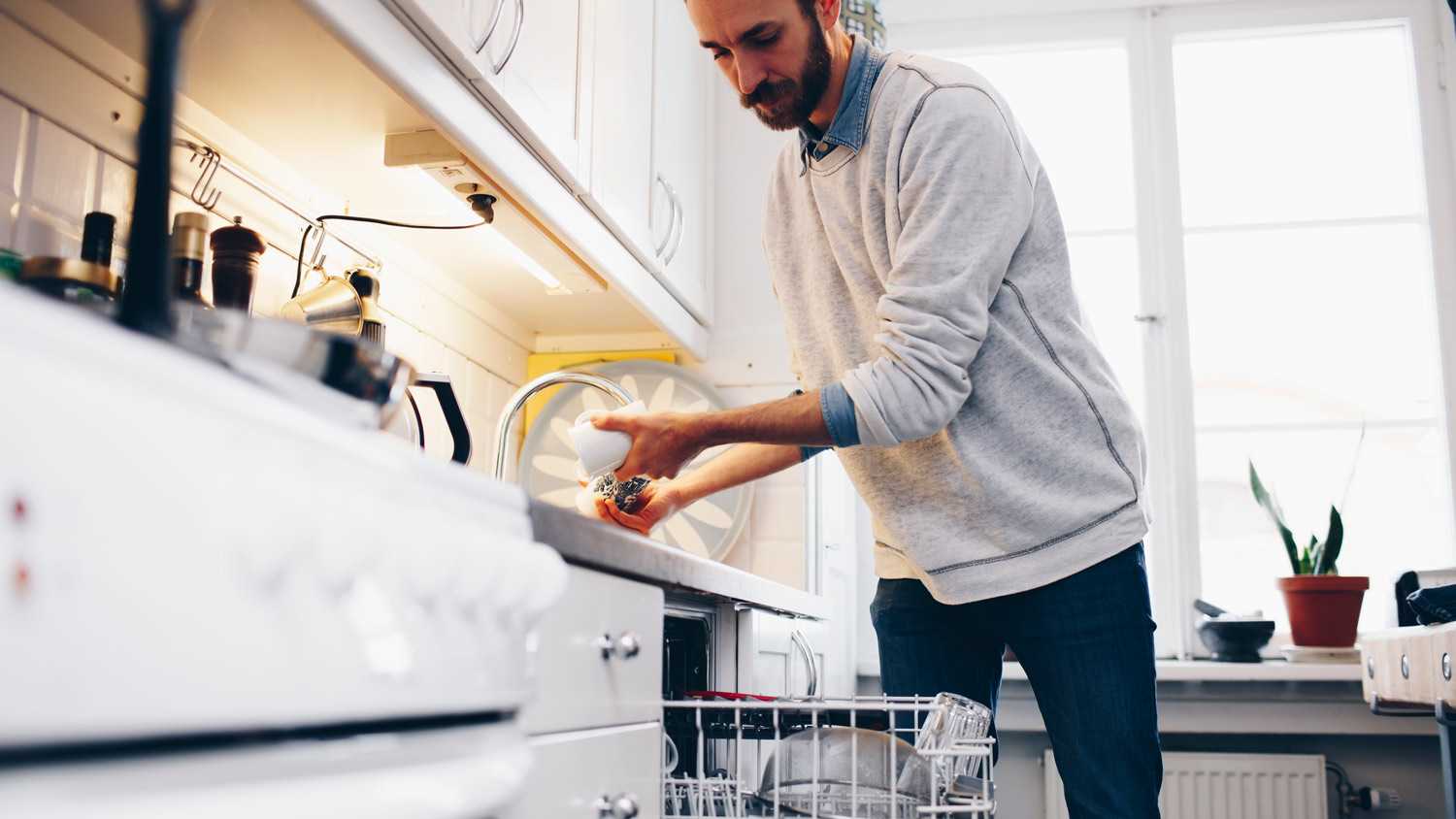 A man rinsing a cup before placing it in dishwasher