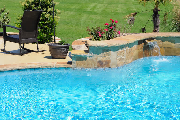 closeup of swimming pool with stone edge, concrete patio, and black lawn chair