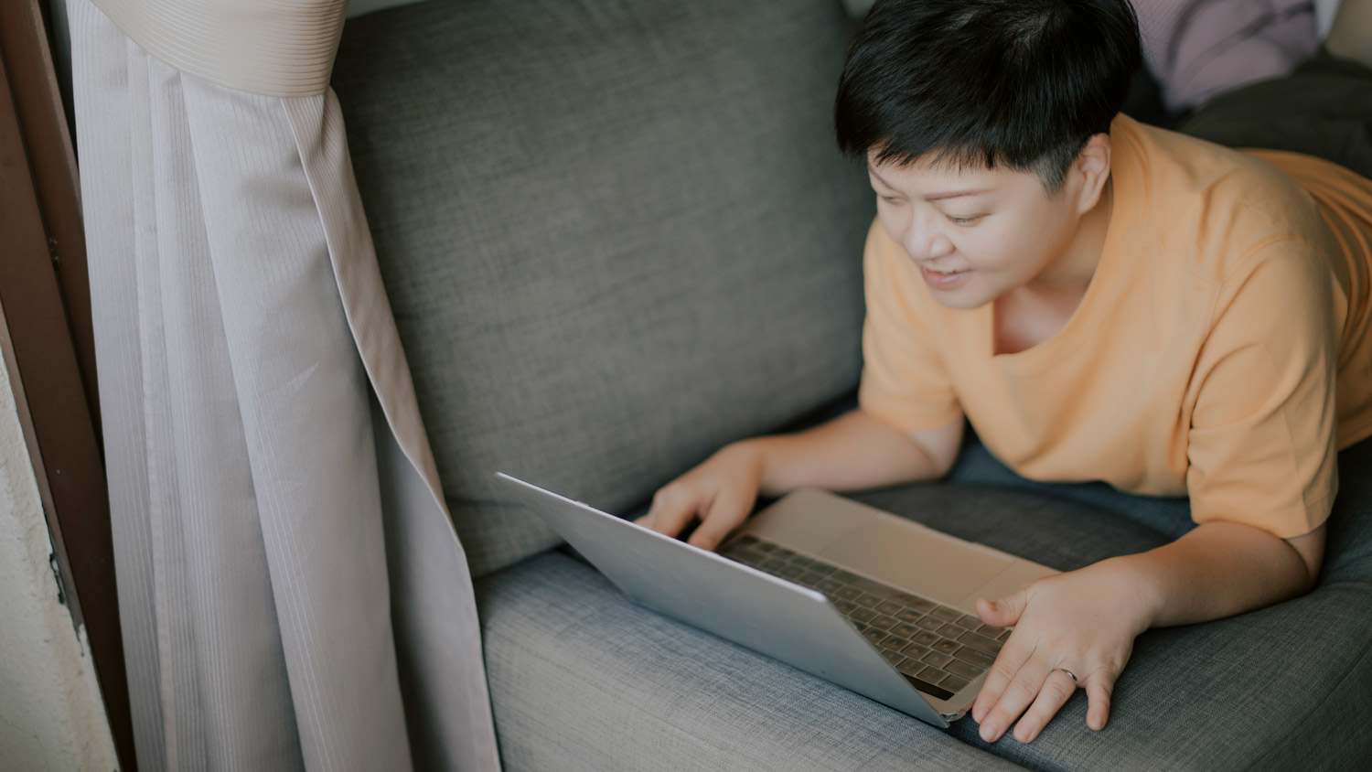 A woman laying on her sofa writing on her laptop