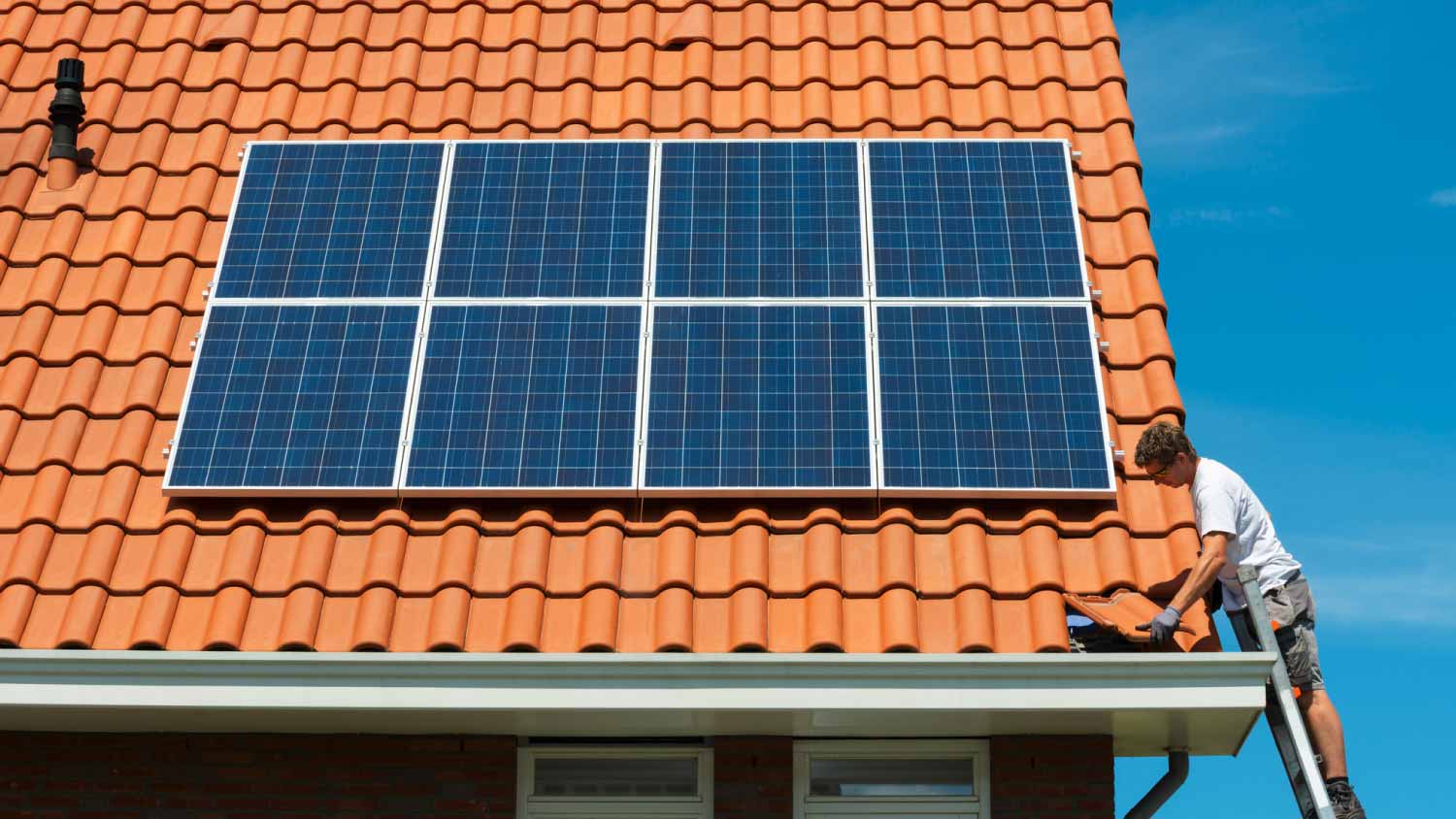 Worker removing roof tile near solar panels