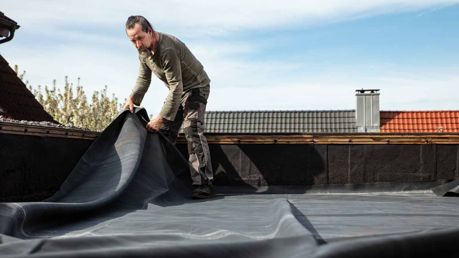 Worker rolling out a thick rubber tarpaulin on a roof