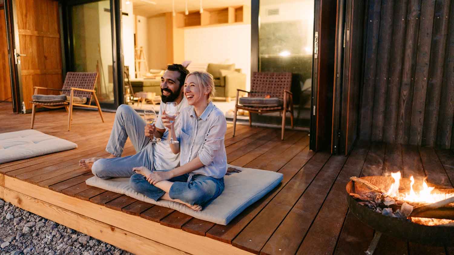 Couple sitting on a deck by fire pit drinking wine