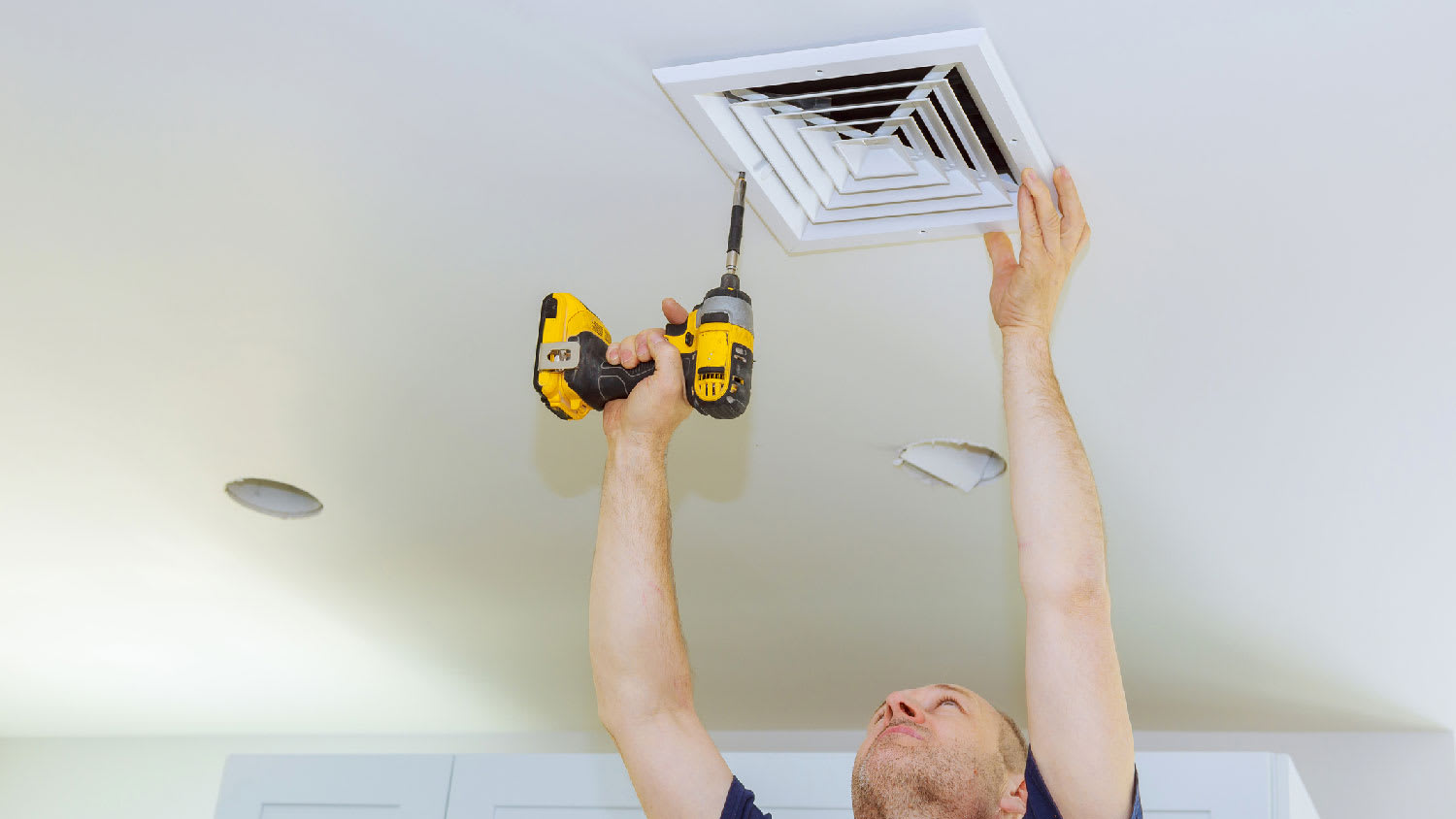 None A person unscrewing an air vent to inspect an air duct