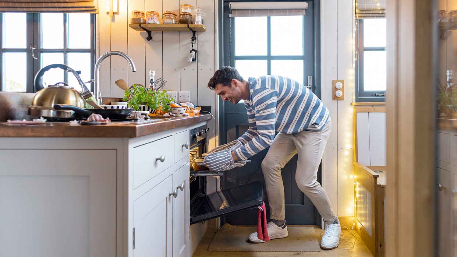 Smiling young man putting baking tray in the oven