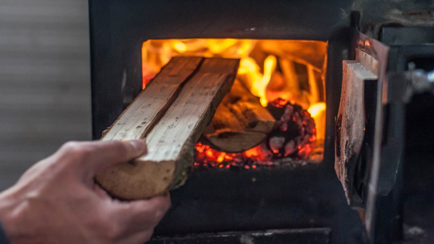 man putting log in wood stove