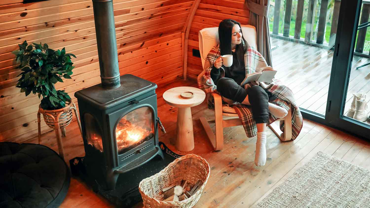 Woman sitting near a wood stove is reading a book